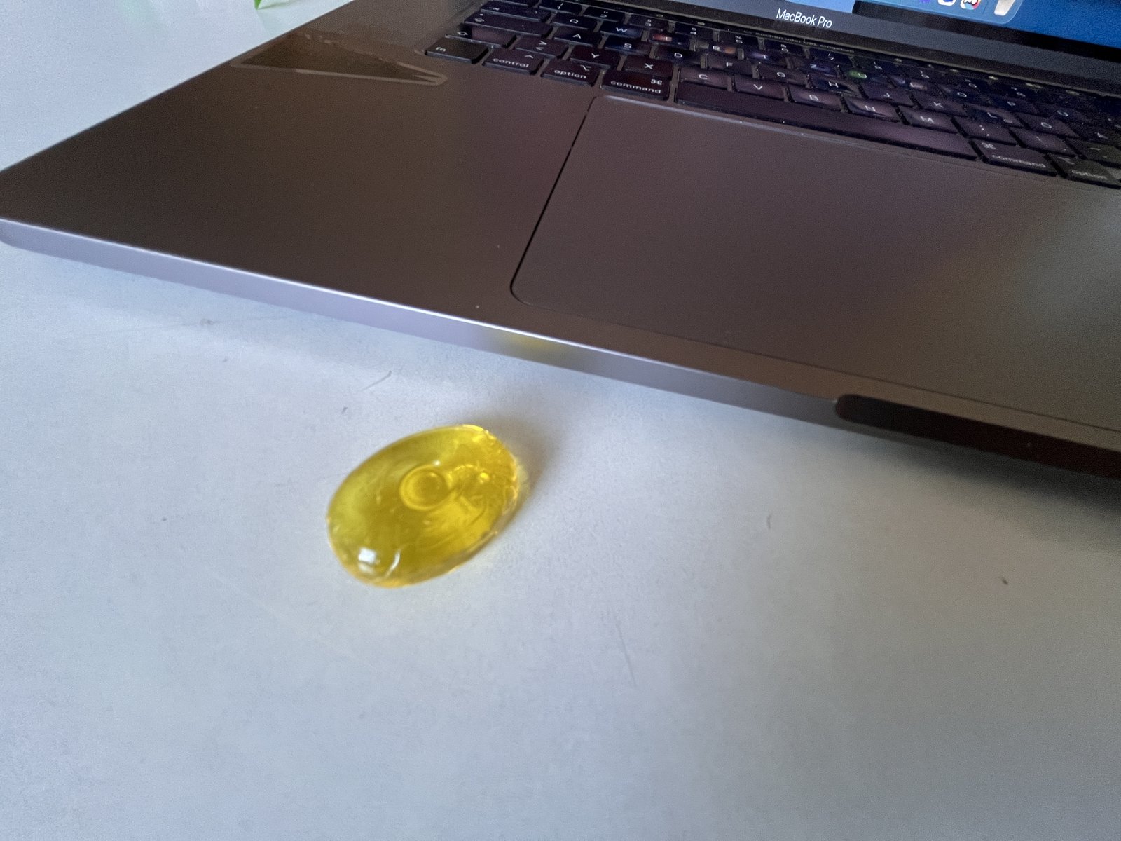 A yellow candy lies on a white table, right next to the palm rest of an open MacBook Pro